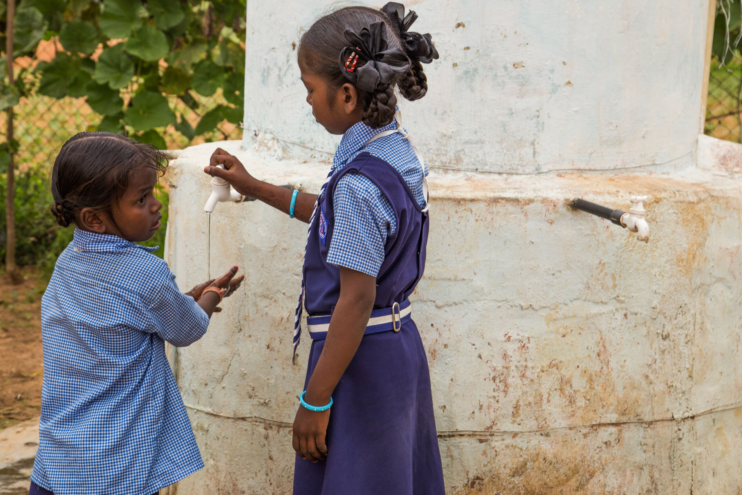 young children in school uniforms enjoy clean well water provided by faithful donors